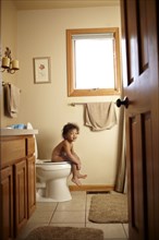 Nude mixed race toddler using toilet