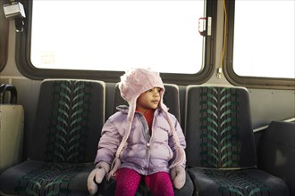 Mixed race girl in hat and gloves riding bus
