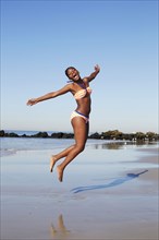 Black woman jumping for joy on beach
