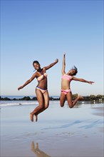 Black women jumping for joy on beach