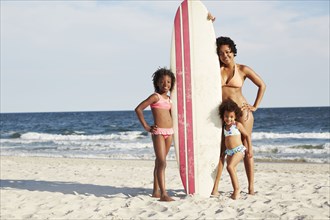 Mother and daughters with surfboard on beach