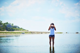 Black teenage girl taking photograph on beach