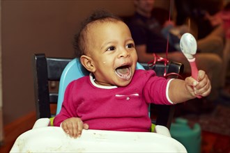 Mixed race girl playing with spoon in high chair