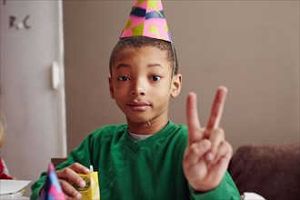 Black boy wearing party hat making peace sign