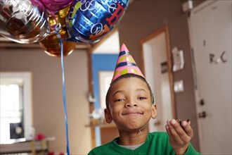 Black boy wearing party hat holding balloons