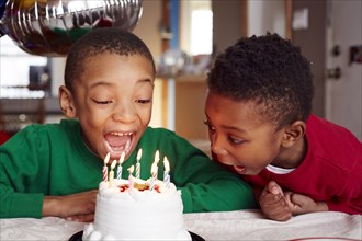 Black boys blowing out cake candles at party