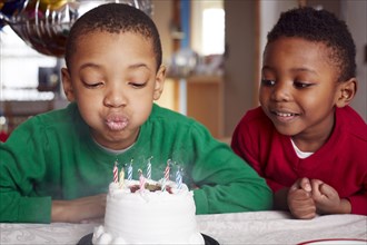 Black boy blowing out cake candles at party