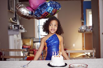 Mixed race girl with balloons and cake at party