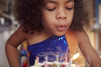 Mixed race girl blowing out cake candles