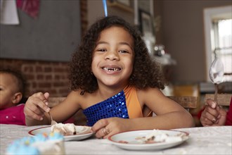 Mixed race girl eating cake at table
