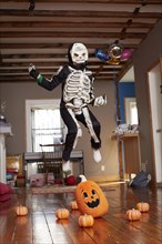 Black boy jumping over pumpkin in skeleton Halloween costume
