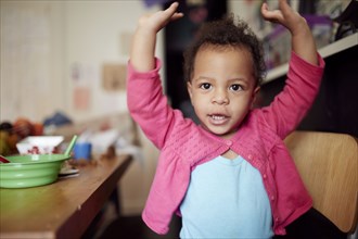 Mixed race baby girl with arms raised at table