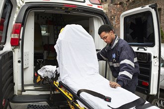 Mixed race paramedic rolling gurney from ambulance