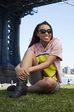 Smiling Black woman sitting in grass at waterfront