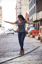 Black woman balancing on track in cobblestone city street