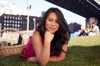Pacific Islander woman laying on grass with picnic basket