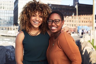 Black women hugging and smiling at waterfront