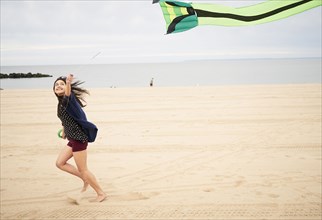 Mixed Race woman running on beach flying kite