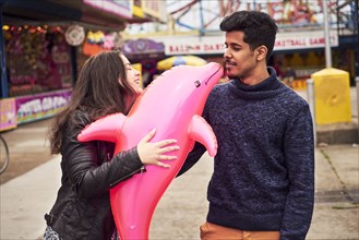 Woman making man kiss inflatable pink dolphin at amusement park