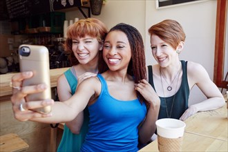 Smiling women posing for cell phone selfie in coffee shop