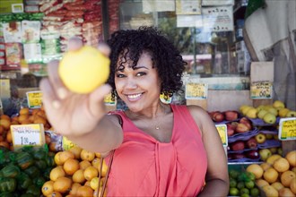 Smiling woman showing lemon at fruit stand