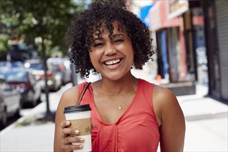 Smiling woman carrying coffee on city sidewalk