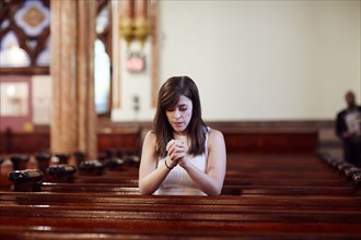 Kneeling Caucasian woman praying in church pew