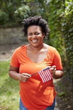 Portrait of laughing Black woman holding little American flag