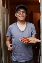 Smiling Japanese man holding plate of raw meat in doorway
