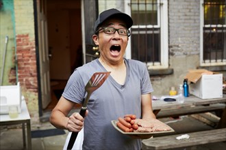 Surprised Japanese man holding plate of raw meat in backyard