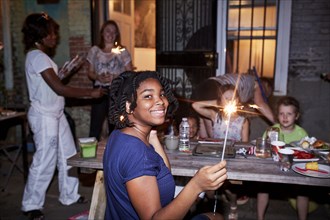 Smiling girl holding burning sparkler at backyard party