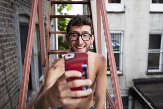 Caucasian man on urban fire escape posing for cell phone selfie
