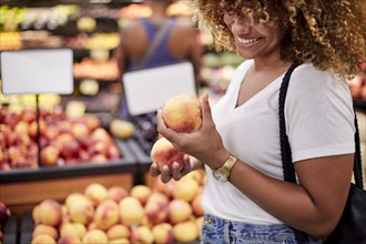 Black woman examining peaches in grocery store