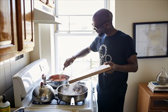 Black man holding cutting board cooking on stove