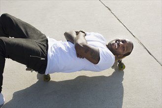 African American man laying on skateboard on city street
