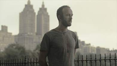 Caucasian runner listening to earbuds in front of city skyline