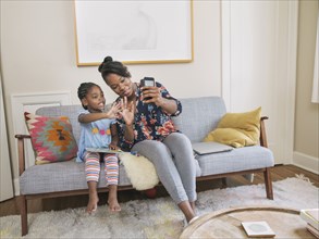 African American mother and daughter taking selfie in living room
