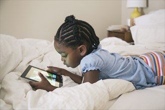 African American girl using digital tablet on bed