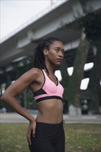 Serious Mixed Race woman wearing pink sports-bra near bridge