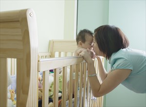 Asian mother and baby touching noses over crib