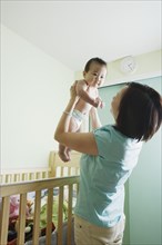 Asian mother lifting baby out of crib