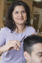 Hispanic female hairstylist cutting hair