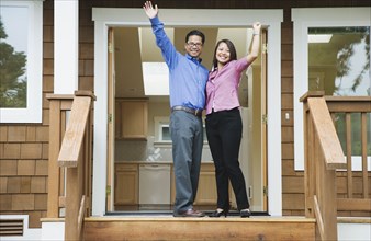 Asian couple waving in front of new house