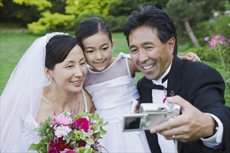 Asian newlyweds and daughter taking own photograph