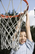 Asian boy hanging from basketball hoop