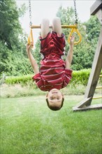 Asian boy hanging upside down on play structure
