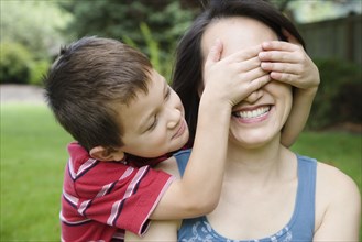 Asian boy covering mother's eyes