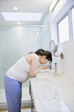 Pregnant Asian woman washing face in bathroom