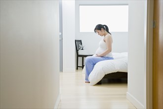 Pregnant Asian woman sitting on bed