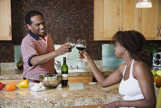 African couple toasting with red wine in kitchen